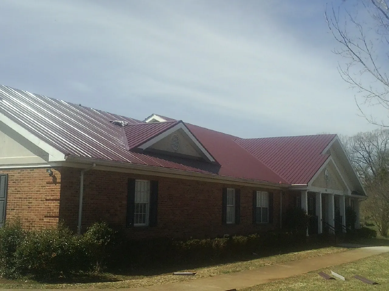 Red metal roof with gabled entries on a long brick building, from a Hail Damage Roof Repair job in Point Pleasant