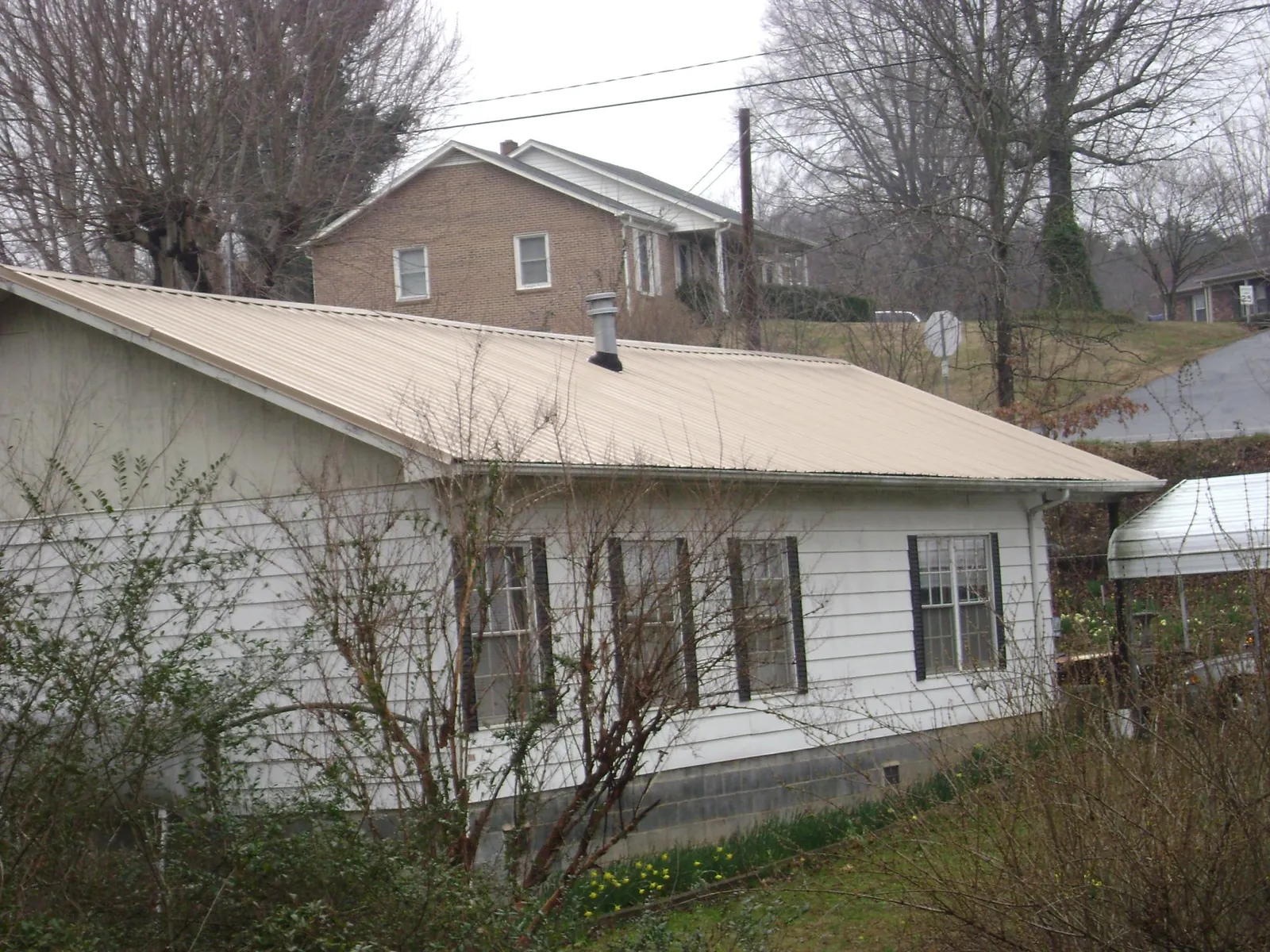 Tan metal roof on a white sided house set into a hillside — Commercial Roofing by Roofing Brothers in Point Pleasant